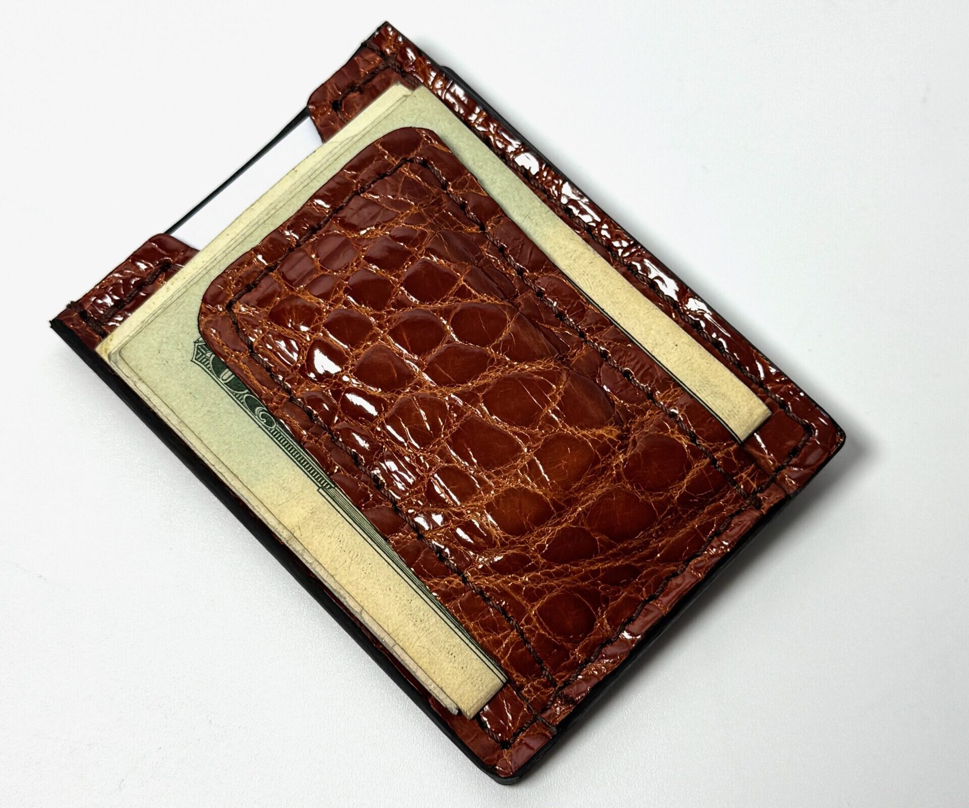 Cognac alligator leather money clip wallet shown from the front with cash secured beneath the center clip.